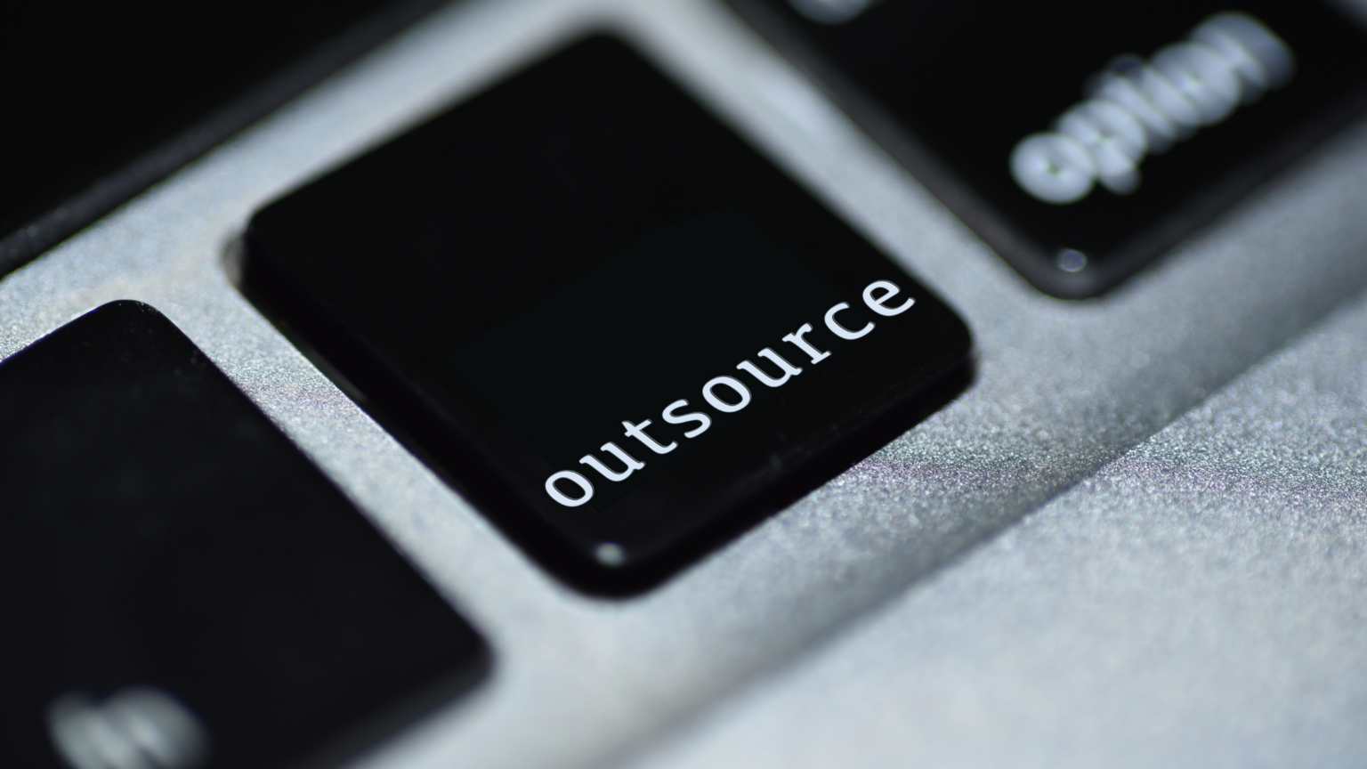 Computer keyboard in black and white with one key showing the word outsource.