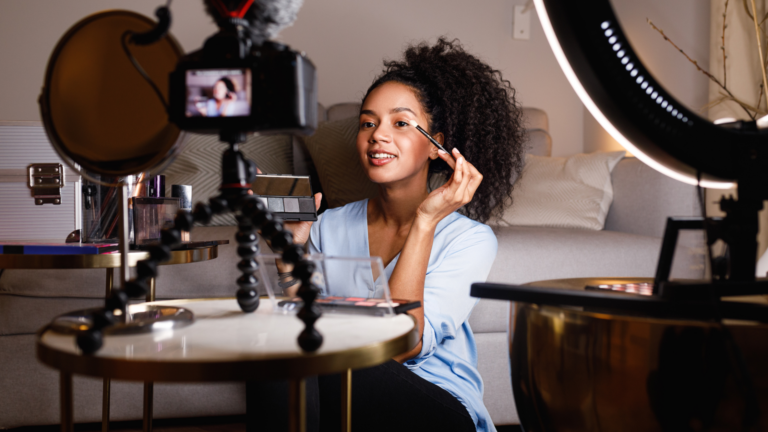 Picture of lady applying make up in front of a camera next to a circular light stand preparing for an influencer marketing campaign