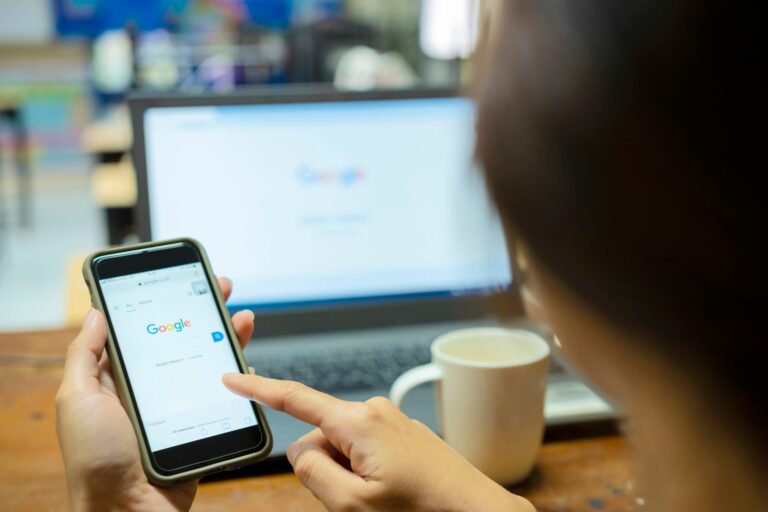 female holding a mobile with google search open and a laptop screen in the background with a google search screen