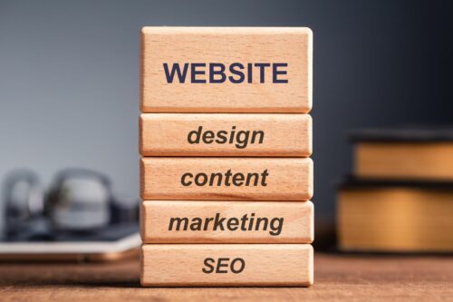 four wooden blocks with SEO, marketing, content, design written on them supporting a bigger block with Website Strategy written on it